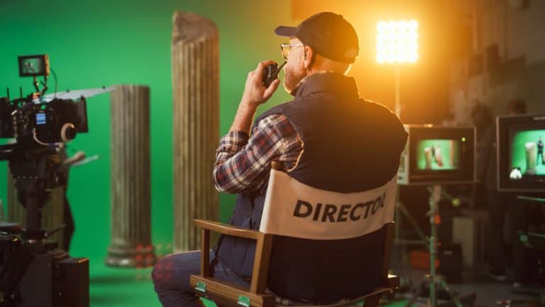 Film director sitting on set in a chair labeled 'Director,' surrounded by cameras and studio lighting