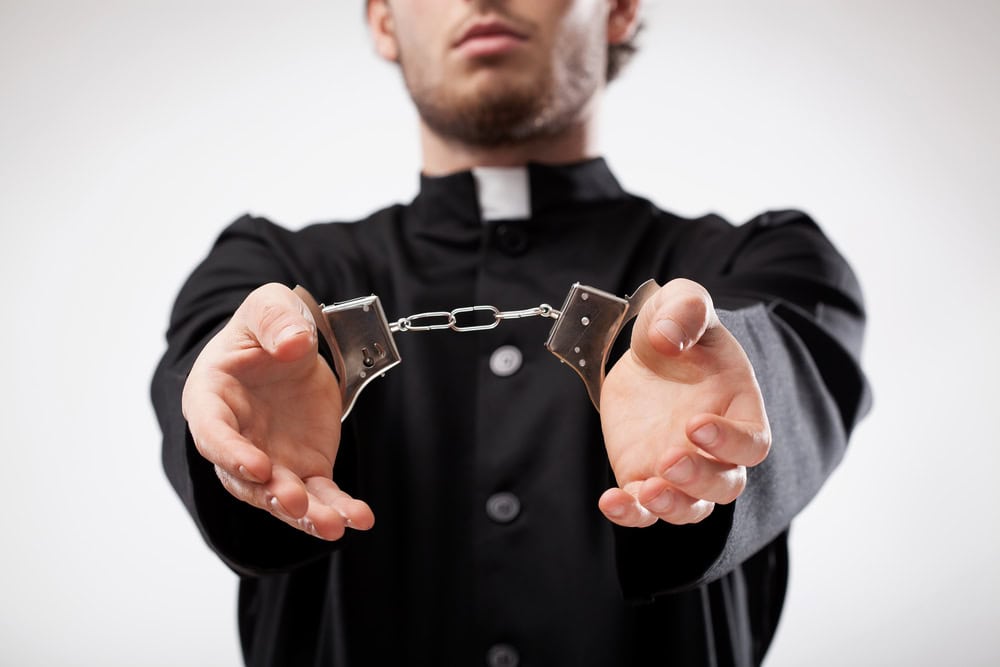 Catholic priest in handcuffs symbolizing criminal prosecution for clergy sexual abuse