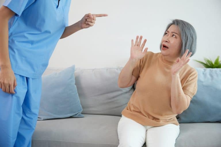 Elderly woman recoiling in fear as a healthcare worker points at her aggressively, symbolizing abuse in a care facility