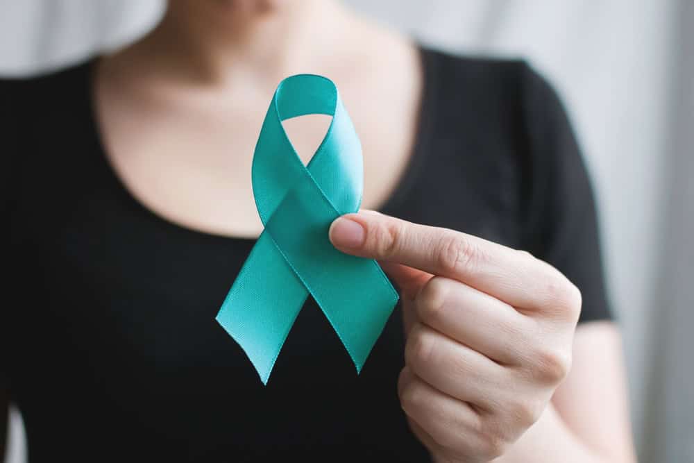 A woman in a black shirt holding a teal ribbon, symbolizing sexual assault awareness and survivor support.