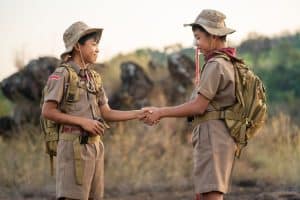 Two boy scouts shake hands in the field.