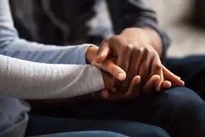 Close up black woman and man in love sitting on couch two people holding hands. Symbol sign sincere feelings, compassion, loved one, say sorry. Reliable person, trusted friend, true friendship concept.