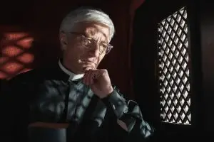 An anonymous priest sits behind the grid of a confessional window looking pensive.