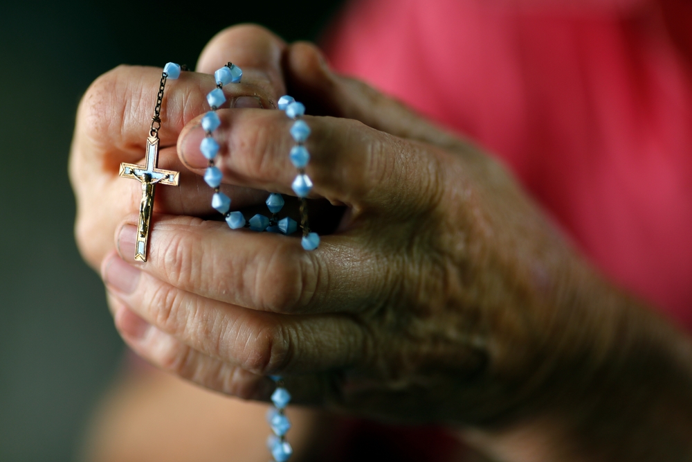 A close-up on the hands of a Catholic man in prayer, gripping the rosary.