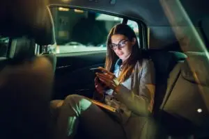 A thoughtful woman holding her phone in a rideshare vehicle at night, symbolizing caution and safety awareness.