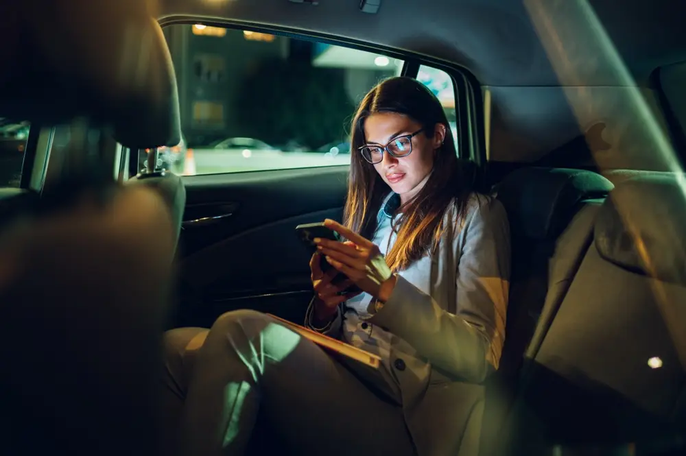 A thoughtful woman holding her phone in a rideshare vehicle at night, symbolizing caution and safety awareness.