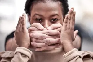 Portrait of a woman with hands covering her mouth, symbolizing silence and suppression in the context of gender-based violence and systemic abuse