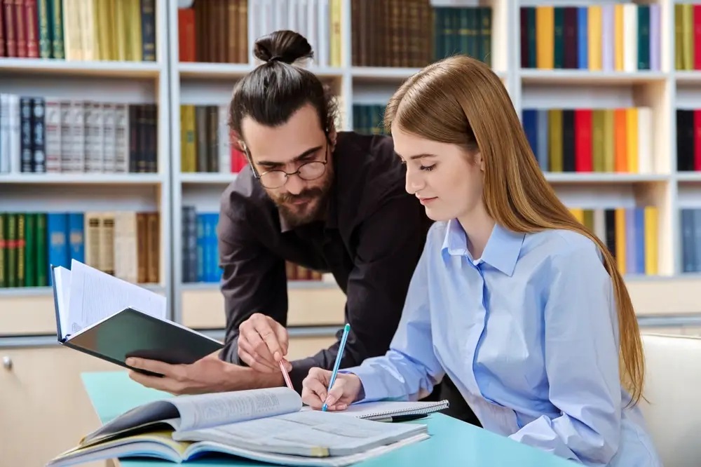 A male teacher assists a teenage female student.