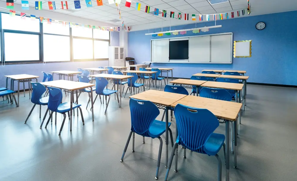 Empty classroom with blue chairs, wooden desks, and international flags hanging from the ceiling.