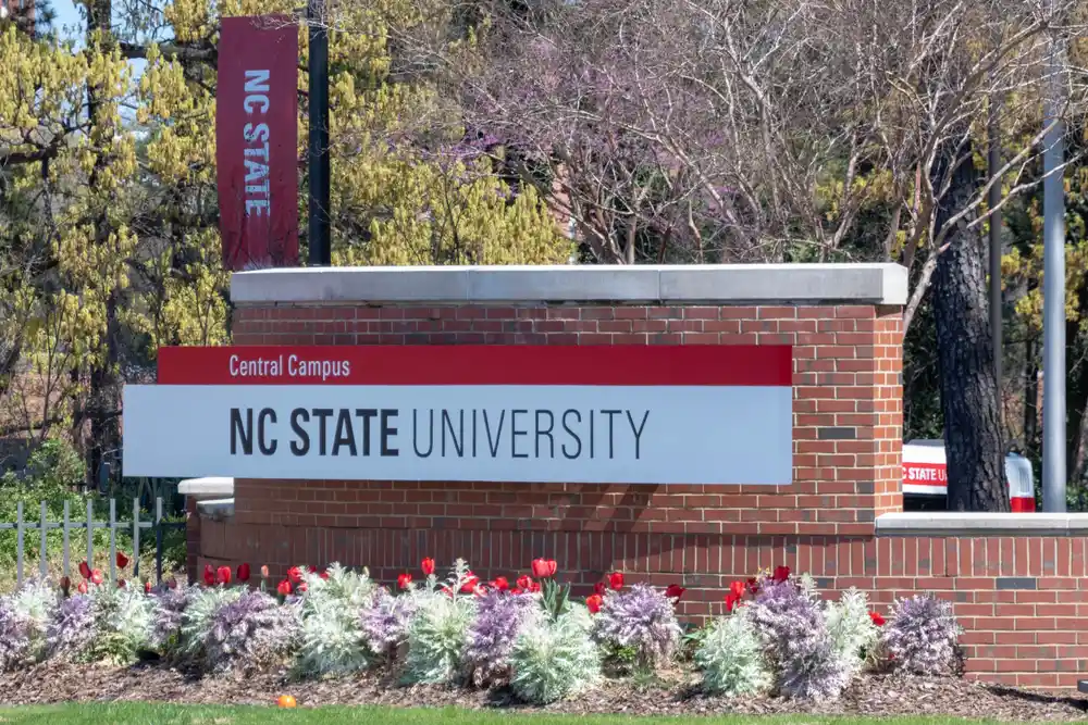 Entrance sign for NC State University Central Campus surrounded by spring flowers and trees.