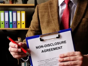 Person in a suit holding a clipboard with a document labeled “Non-Disclosure Agreement,” symbolizing legal restrictions tied to NDAs.