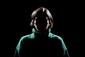 Silhouette of a person in a dark setting with their face obscured, symbolizing survivor privacy and anonymity.
