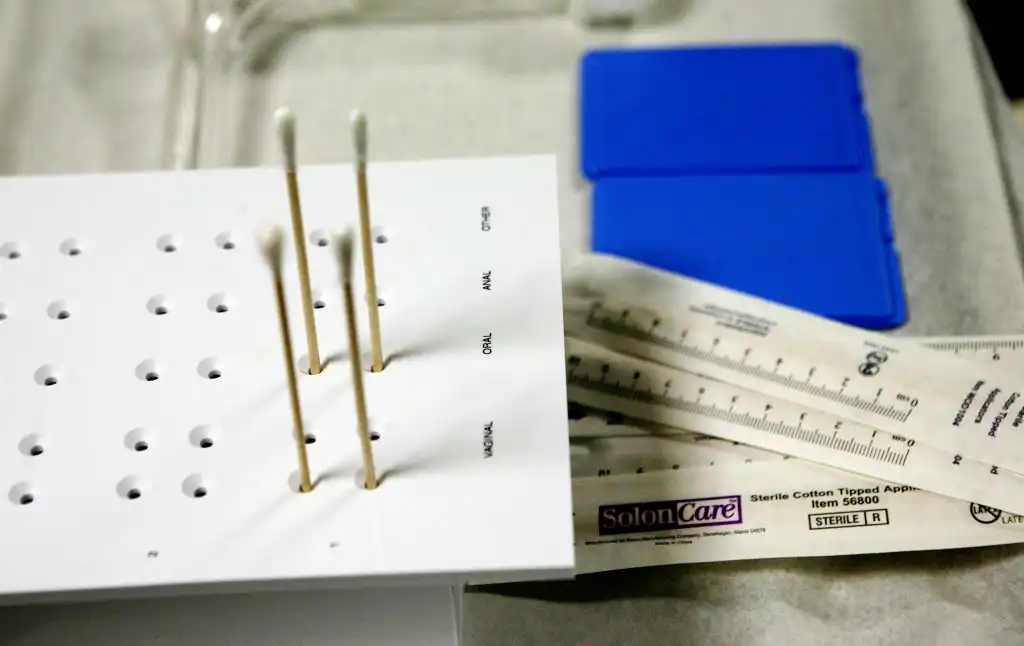 Close-up of a sexual assault forensic evidence kit showing cotton swabs, measuring tools, and labeled collection tray compartments
