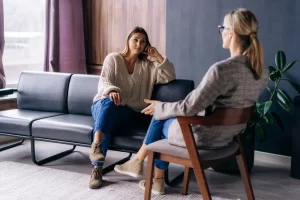 A woman sits in a therapy session with a counselor, symbolizing supportive mental health care for survivors.