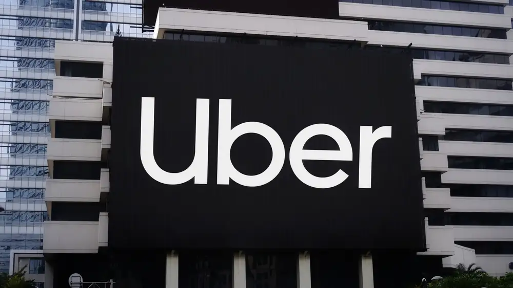 Uber logo displayed on a large black sign attached to the side of a modern corporate building, symbolizing the company’s presence amid legal scrutiny.
