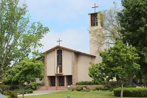 Entrance of the Cathedral of St. Eugene in Santa Rosa, California, featuring twin crosses, a statue of the Virgin Mary above the doorway, and surrounding greenery.