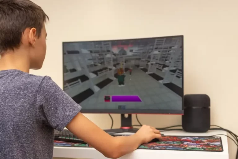Child playing Roblox on a desktop computer, viewed from behind, showing the game interface on screen.