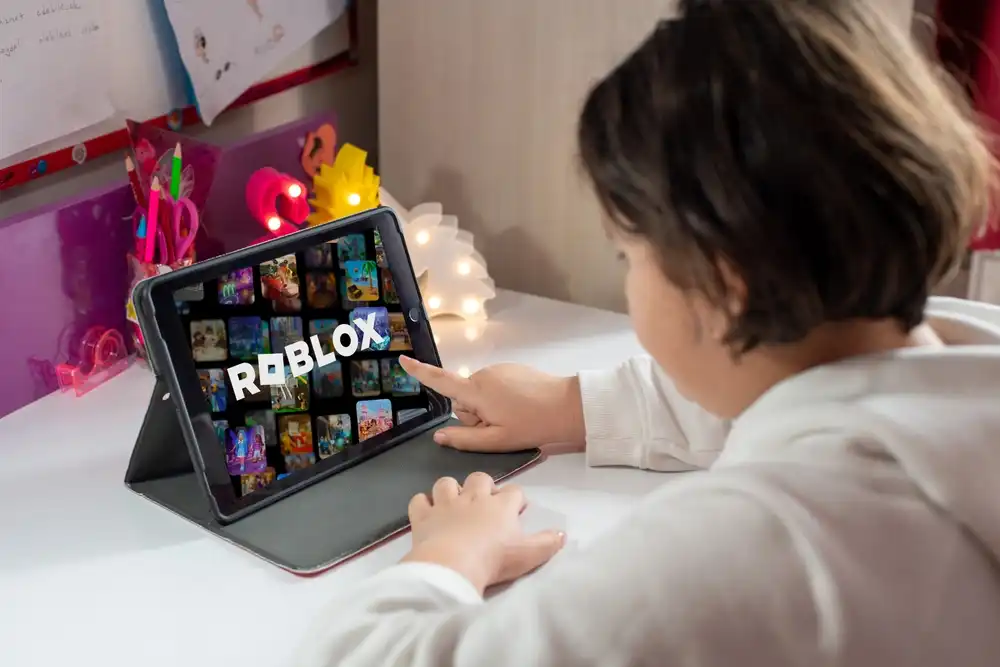 Child using a tablet to play Roblox, an online gaming platform under investigation and facing lawsuits for alleged child exploitation and safety failures.