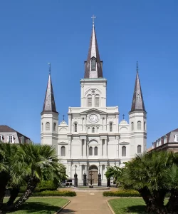 St. Louis Cathedral in New Orleans, featuring three tall spires, white stucco façade, and palm trees in the foreground under a clear blue sky