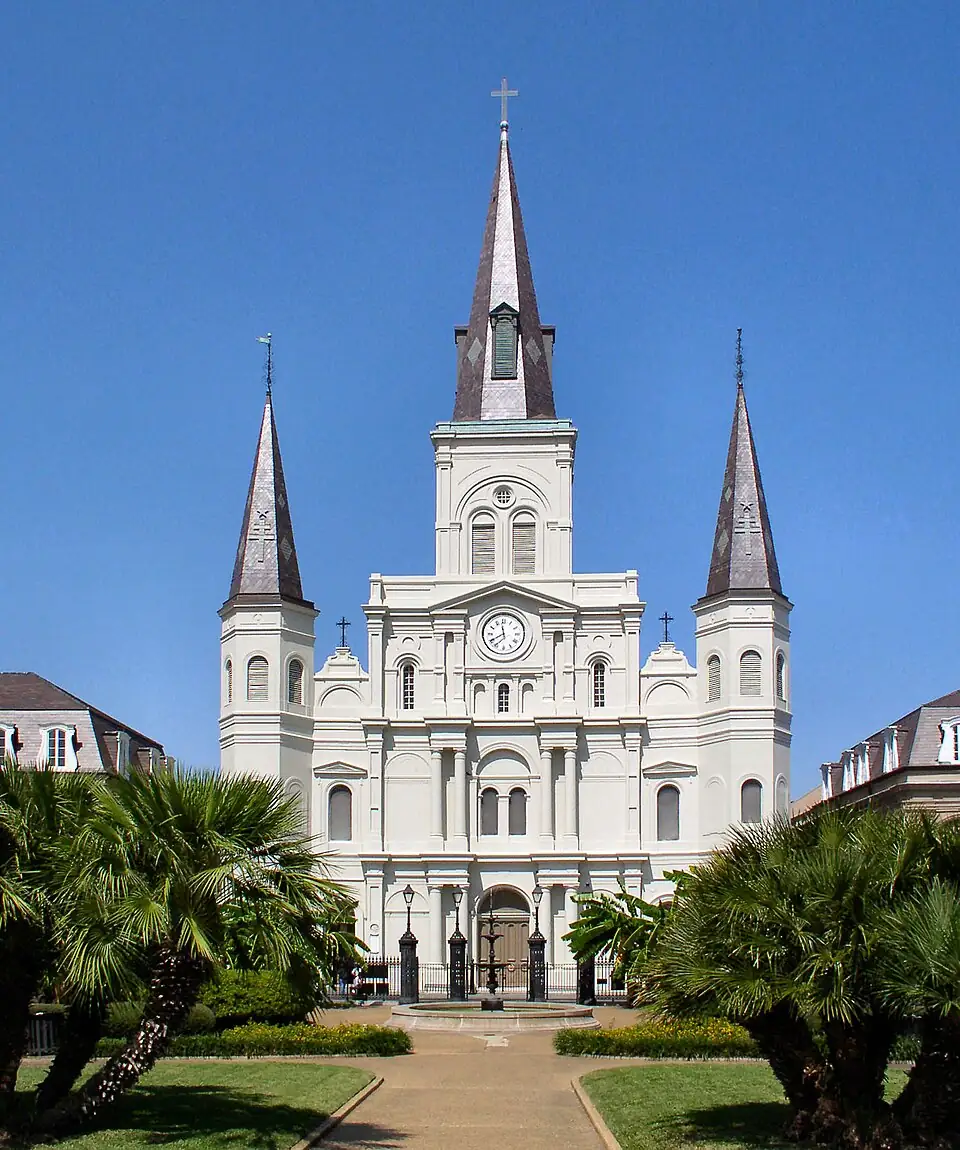 St. Louis Cathedral in New Orleans, featuring three tall spires, white stucco façade, and palm trees in the foreground under a clear blue sky