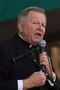 Archbishop of New Orleans Gregory Michael Aymond speaking into a microphone during a public event.