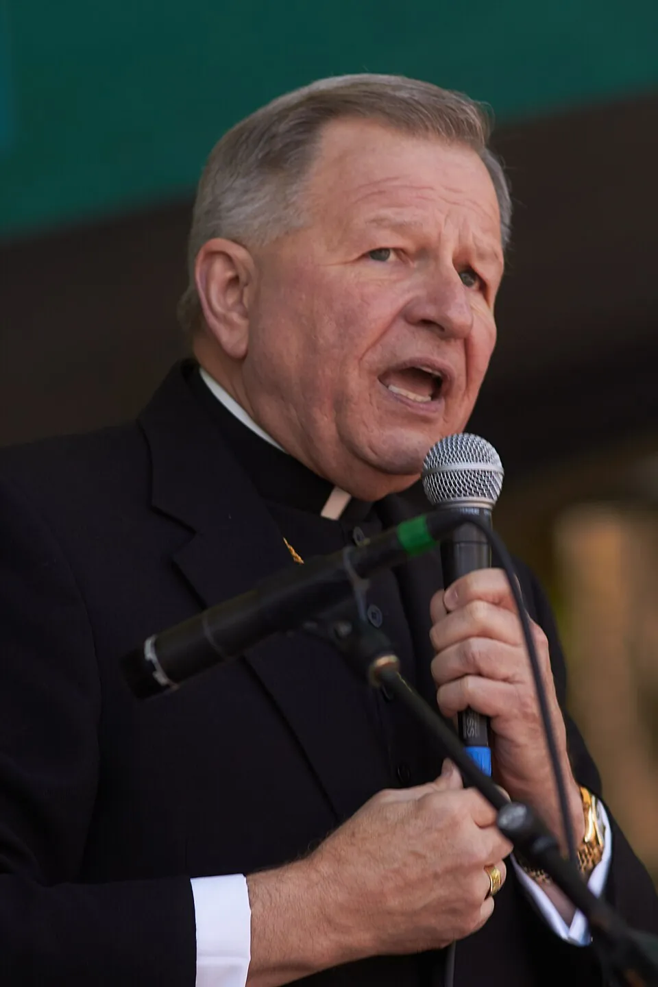 Archbishop of New Orleans Gregory Michael Aymond speaking into a microphone during a public event.