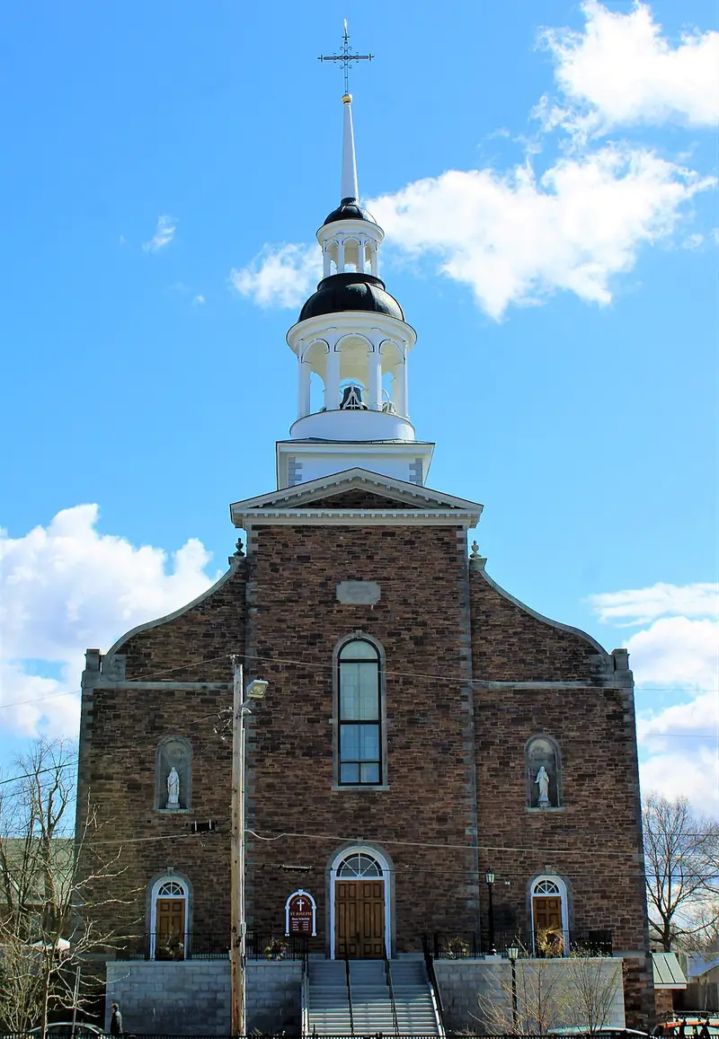 The Cathedral of Saint Joseph in Burlington, Vermont, featuring a stone façade, tall central steeple with a cross, and clear blue sky in the background.
