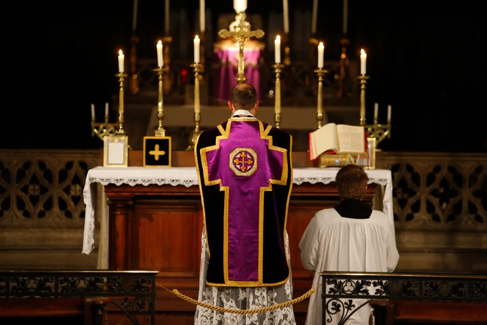 Catholic priest wearing a purple chasuble leads a solemn Mass at the altar.