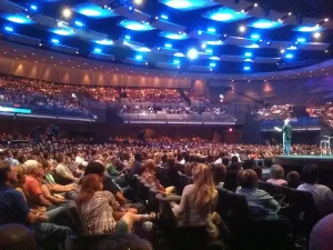 Packed auditorium at Gateway Church in Texas with a pastor speaking on stage before thousands of congregants under bright blue stage lighting.