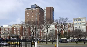 Henry Ford Hospital in Detroit, Michigan, a major medical center with multiple large brick and concrete buildings shown from the street view with cars and trees in front.