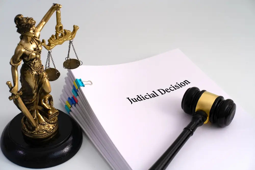 A gavel and Lady Justice statue beside a legal document labeled “Judicial Decision,” symbolizing a courtroom verdict.