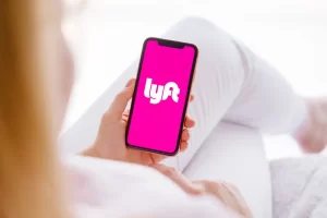 Person holding a smartphone displaying the Lyft app logo on a pink screen, symbolizing the rideshare company at the center of sexual assault lawsuits