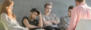 A group of teenagers sit in a therapy circle, appearing withdrawn and distrustful, symbolizing the emotional toll of life inside troubled teen programs
