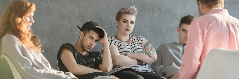 A group of teenagers sit in a therapy circle, appearing withdrawn and distrustful, symbolizing the emotional toll of life inside troubled teen programs
