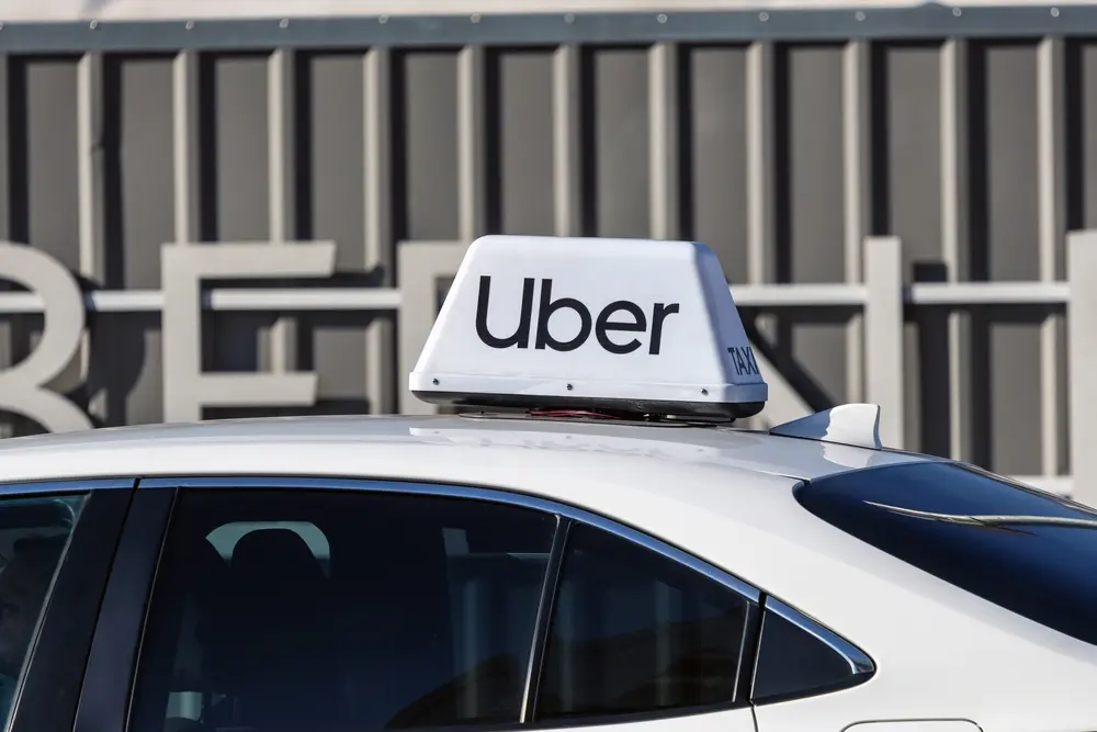 Uber sign mounted on top of a white car parked outside a building.