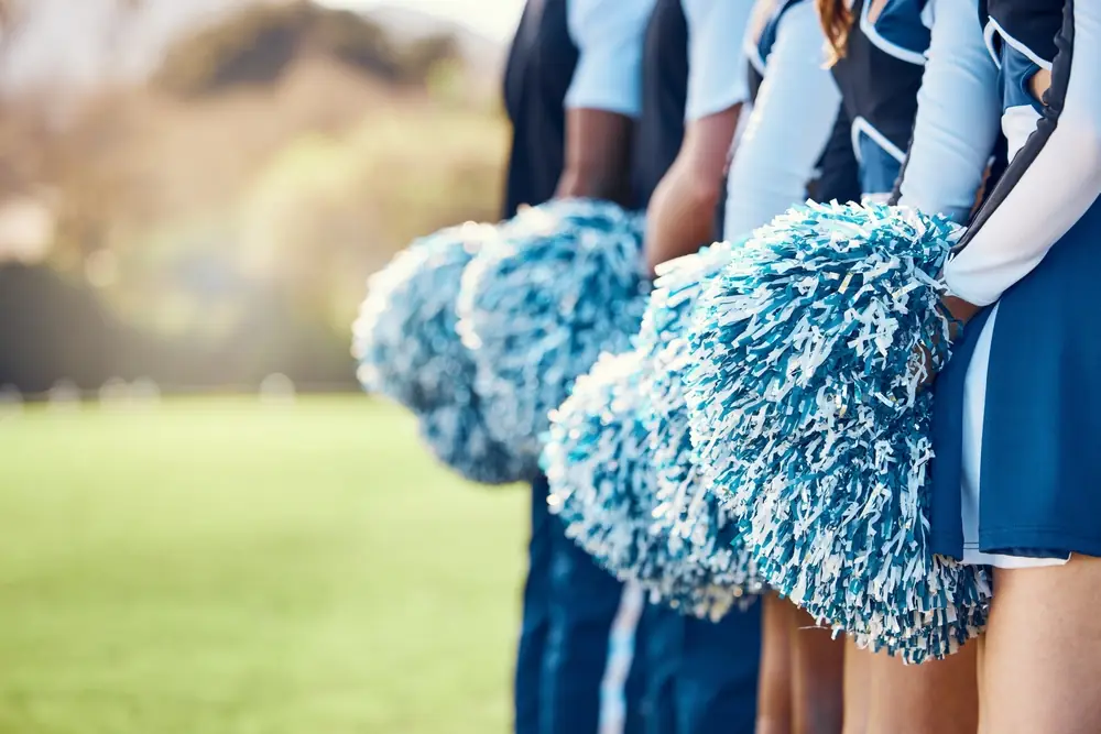 Close-up of cheerleaders in uniform holding blue and white pom-poms on a field, representing the competitive cheerleading community.