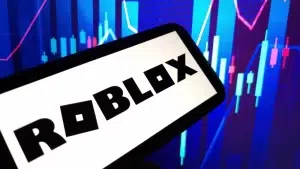 A smartphone displaying the Roblox logo in front of a colorful digital chart with rising and falling candlestick graphics.