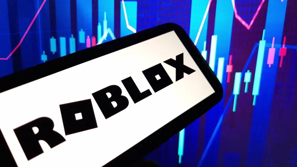 A smartphone displaying the Roblox logo in front of a colorful digital chart with rising and falling candlestick graphics.
