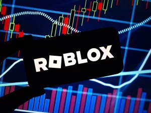 A silhouette holding a Roblox logo in front of a background of colorful financial charts and digital market graphics.