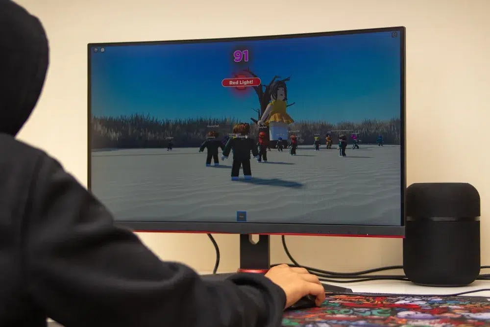 Person playing a Roblox game on a desktop monitor, showing a “Red Light” scene with multiple on-screen characters.