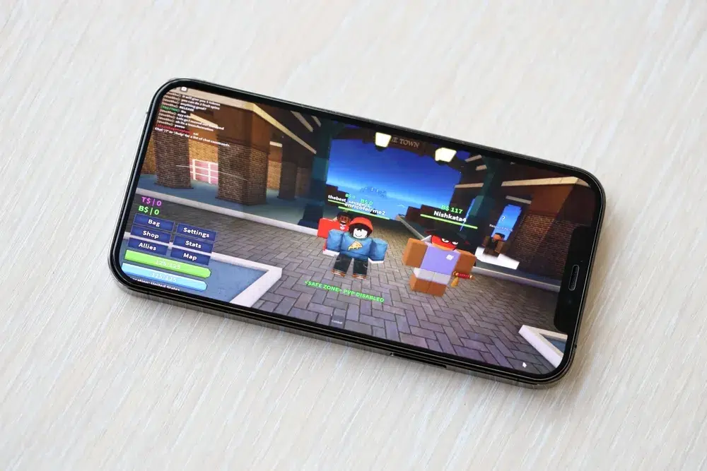 Smartphone displaying Roblox gameplay with multiple characters in a virtual town, illustrating concerns about child safety on the Roblox platform.