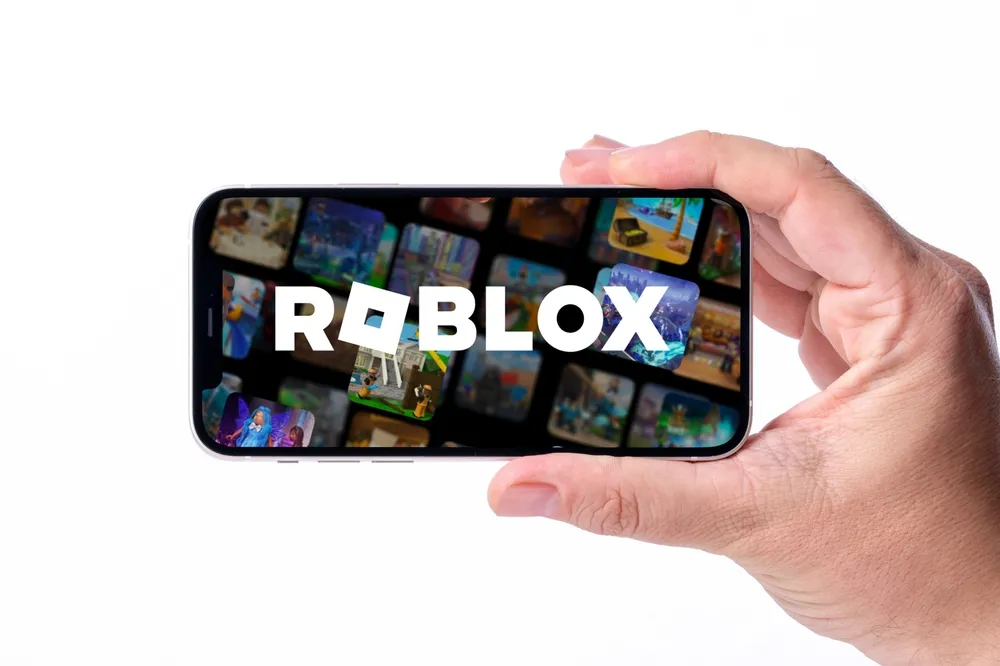 A person holding a smartphone displaying the Roblox logo on the screen, representing online gaming and child safety concerns on the platform.