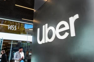 The Uber logo displayed on the exterior wall of a corporate office building, with people standing near the entrance.