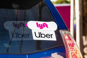 Rear window of a blue car displaying both Uber and Lyft decals, representing a vehicle used for rideshare driving.