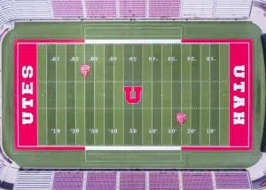 Overhead aerial view of the University of Utah football field at Rice-Eccles Stadium, showing the red end zones labeled UTES and UTAH with the large block U logo at midfield.