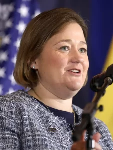 Iowa Attorney General Brenna Bird speaking at a podium with an American flag visible in the background.