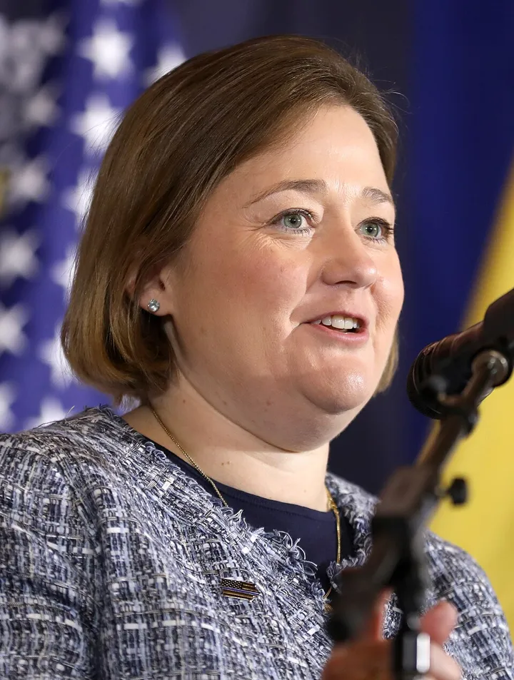 Iowa Attorney General Brenna Bird speaking at a podium with an American flag visible in the background.