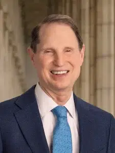 U.S. Senator Ron Wyden wearing a blue suit and light blue tie, photographed inside a government building.
