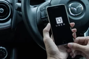 Close-up of an Uber driver holding a smartphone with the Uber app open while sitting behind the wheel of a car.