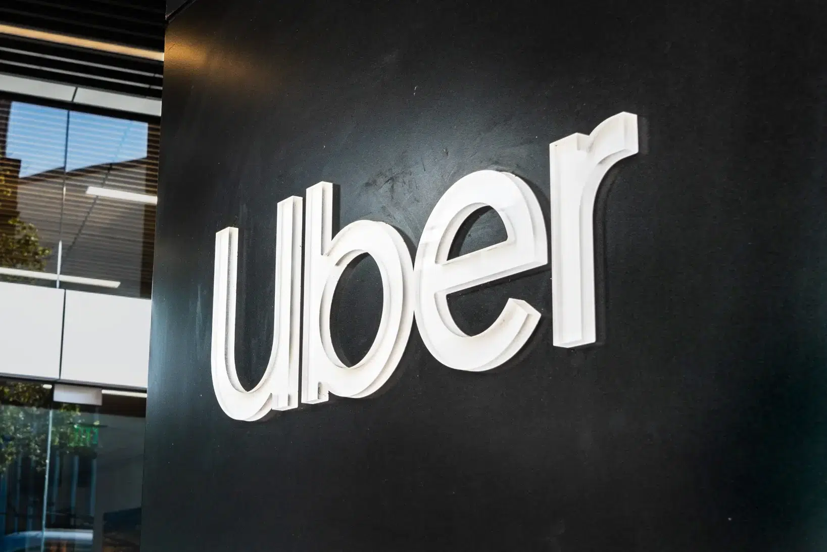 Uber corporate logo displayed on a dark wall inside a modern office building.